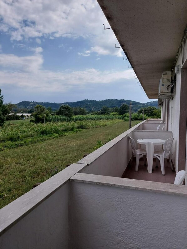 A balcony with a table and chairs, overlooking a grassy area and distant hills. - La Lanterna (Santi Cosma e Damiano)
