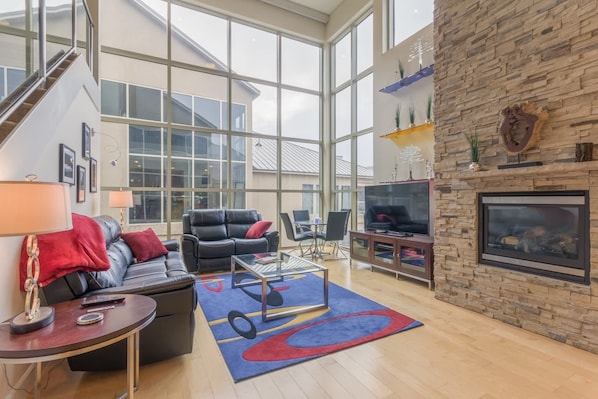 A spacious living room with a large window, a fireplace, and a staircase leading to an upper level.