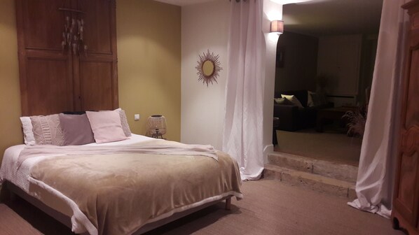 A bedroom with a bed, a wooden wardrobe, a wall-mounted mirror, and a lamp.