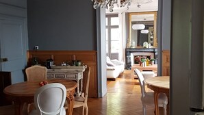 A spacious living area with a wooden herringbone floor, a dining table with white chairs, and a kitchen area with a wooden cabinet and a white sofa. - Les Rives de la Tronne (Mer)
