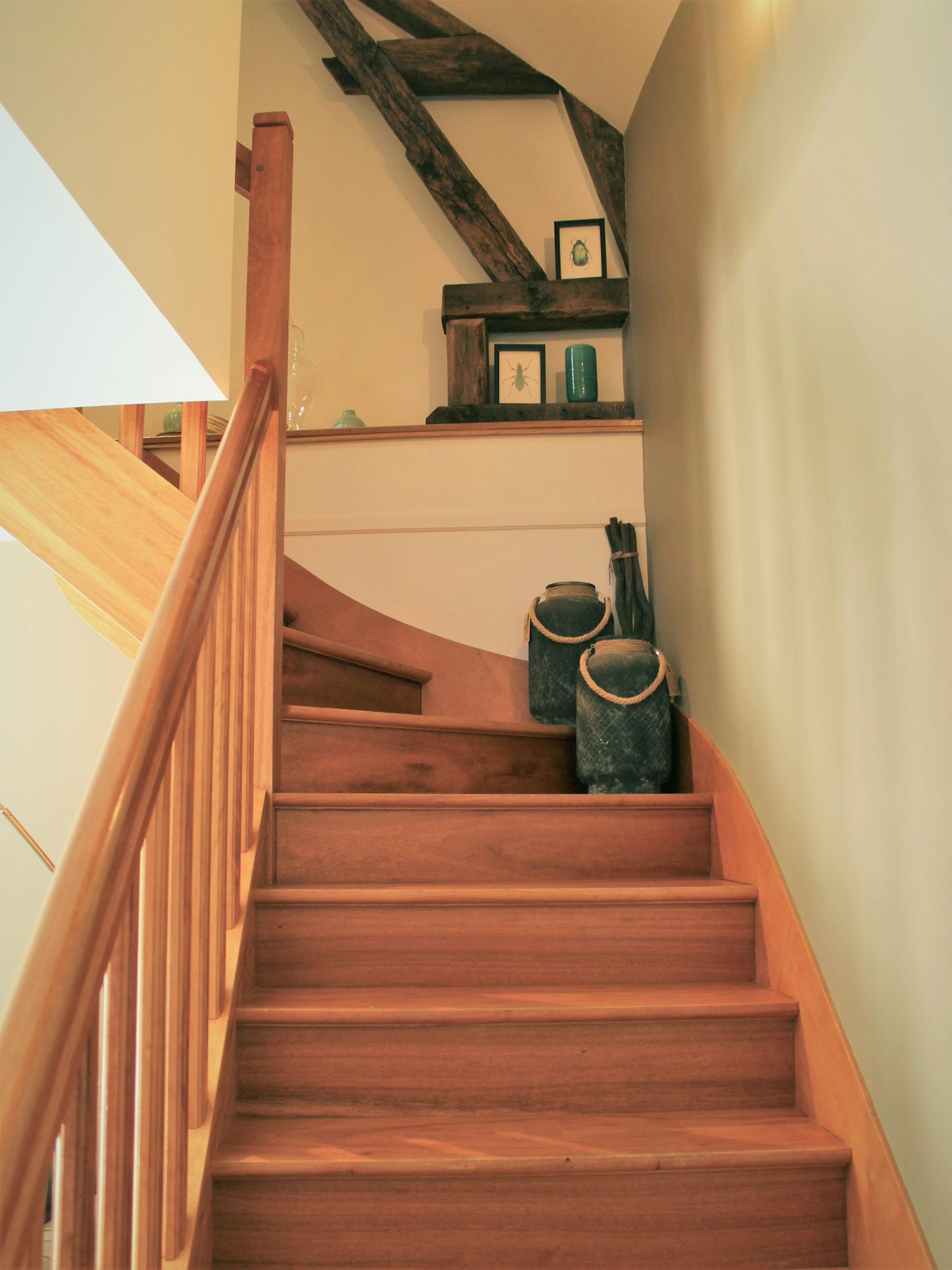 A wooden staircase with a handrail, a wooden beam structure above, and two trash bins on the landing.