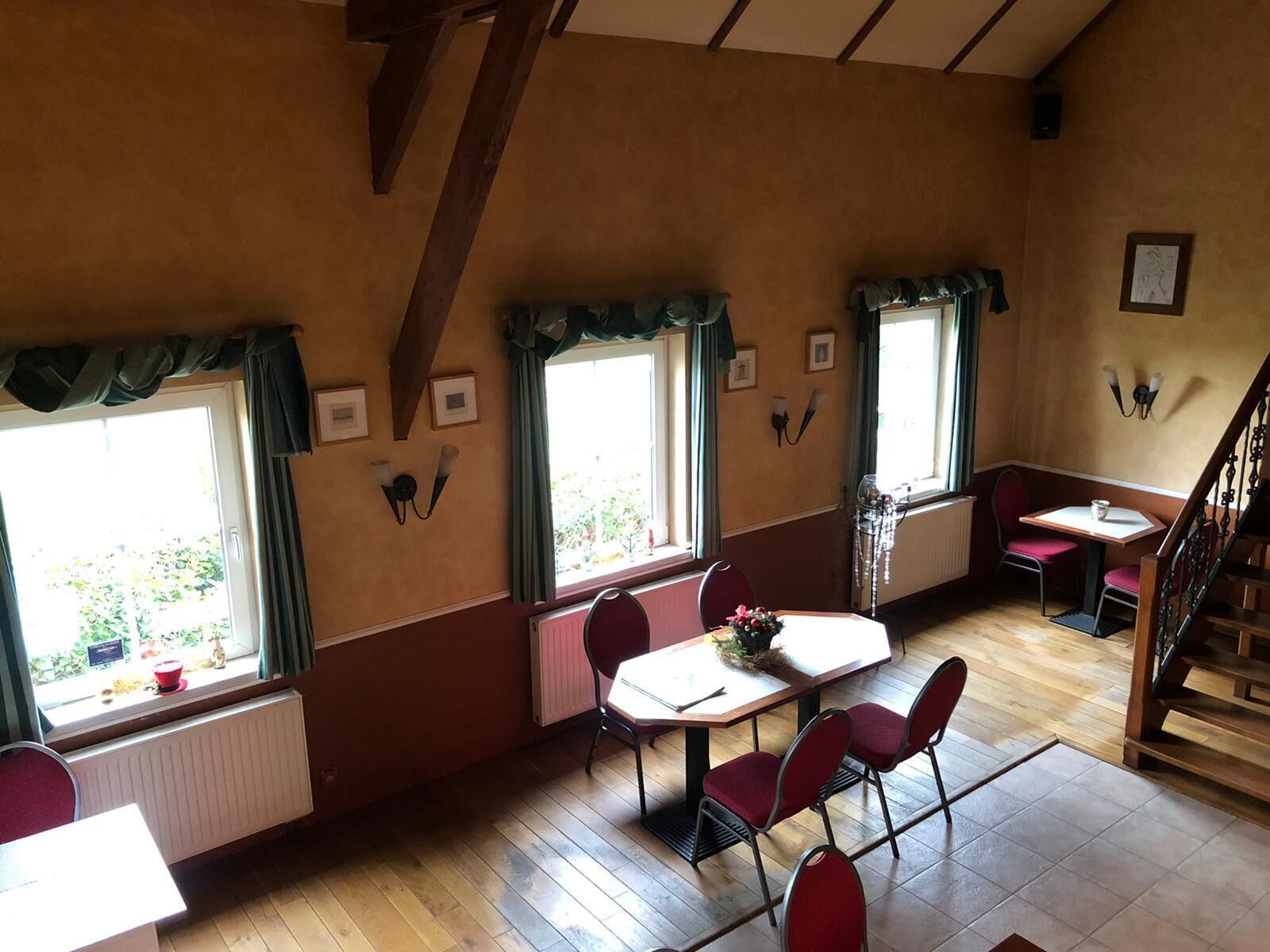 A dining area with a table and chairs, a staircase, and windows with curtains.