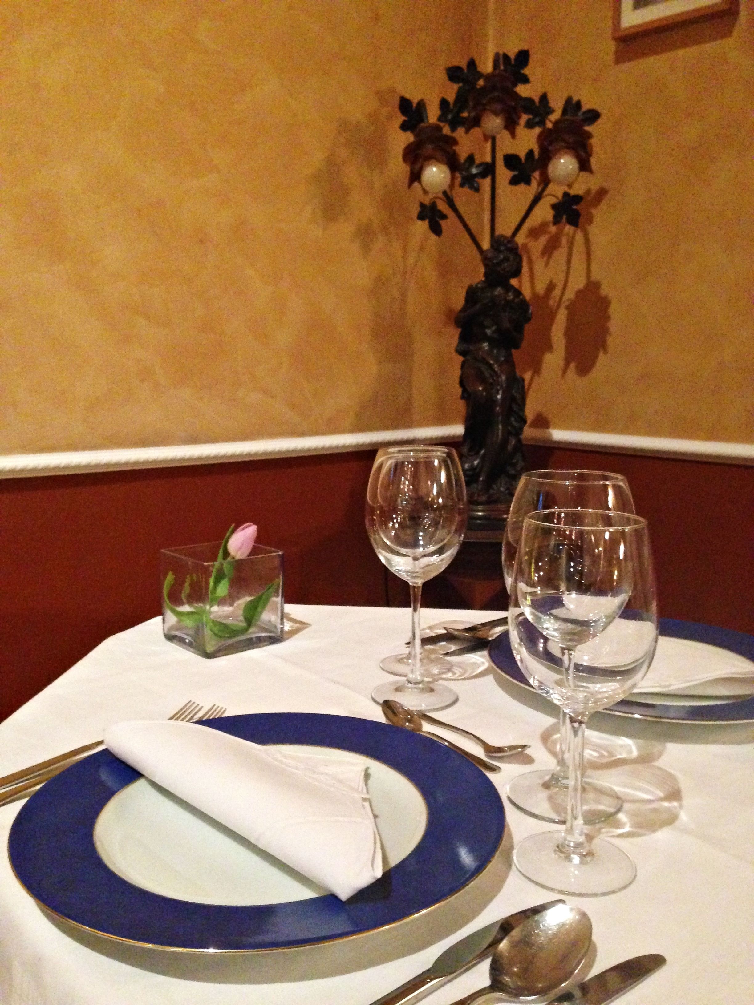 A table set with blue and white plates, silverware, and two wine glasses.
