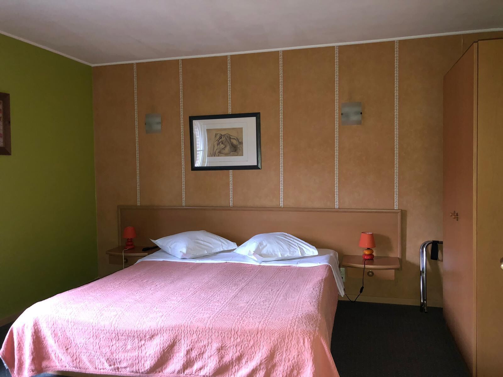 Quarto de hotel com uma cama, duas mesas de cabeceira, um criado-mudo, uma moldura na parede e um guarda-roupa.