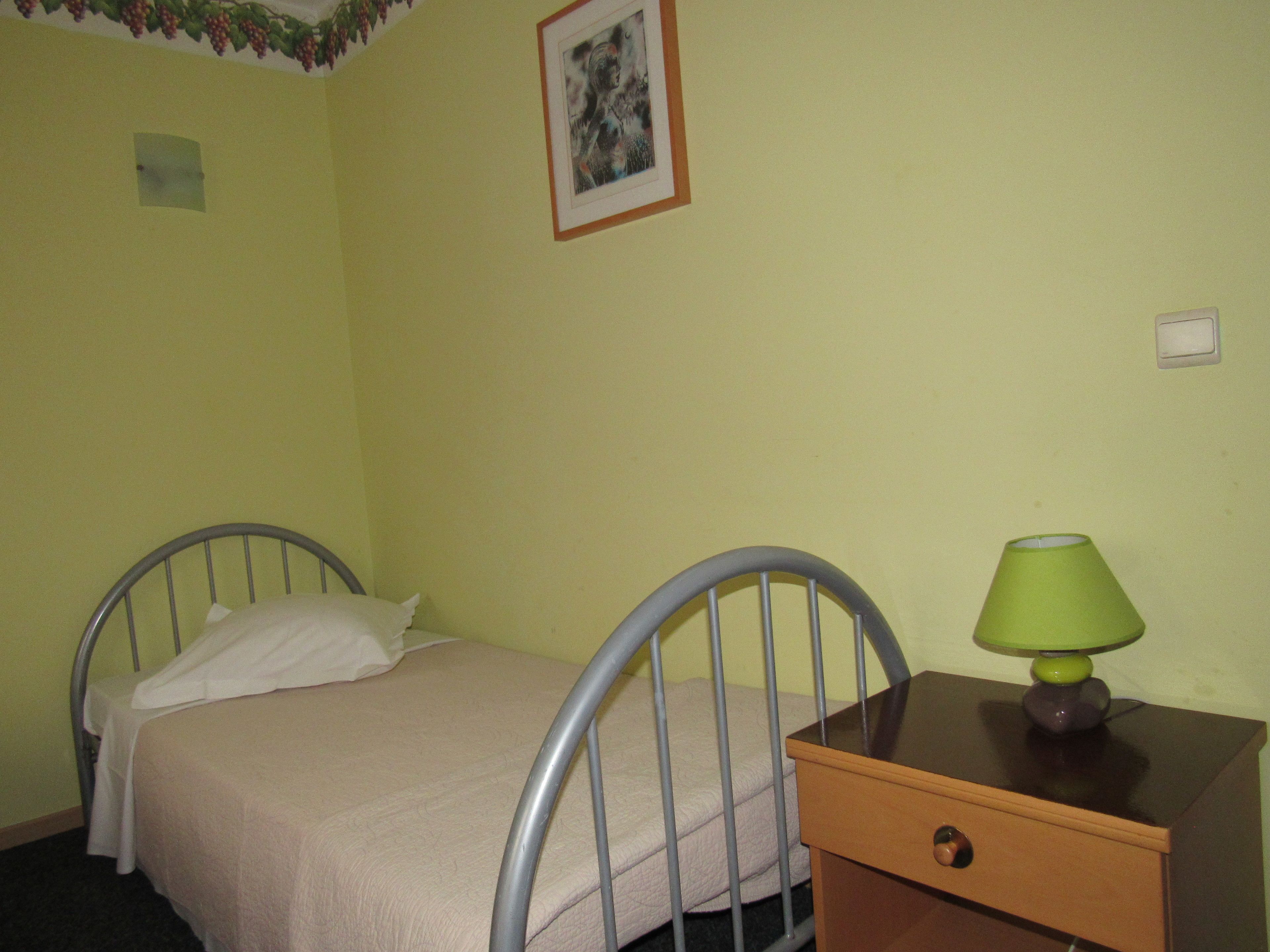A single bed with a metal frame and a wooden nightstand with a green lamp.