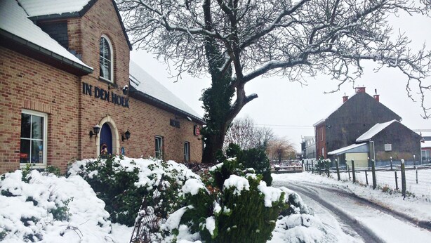 A brick building with a sign reading "IN DEM HOER" and a large tree in front. - Hotel In den Hoek (Tielt-Winge)