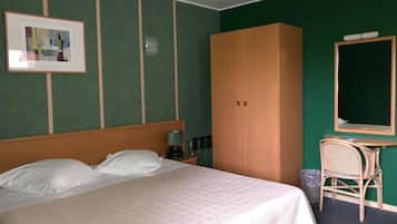 Una habitación de hotel con cama, armario, escritorio con silla y un cuadro en la pared.
