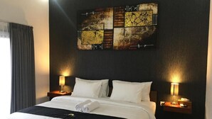 A hotel room with a large bed, two bedside tables with lamps, a dark wall, and a large abstract artwork above the bed. - Jepun Sari Uluwatu (Pecatu)