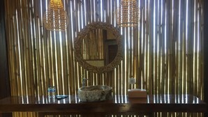 A bathroom with a wooden vanity, a round mirror, two hanging lights, and a bamboo backdrop. - Jepun Sari Uluwatu (Pecatu)