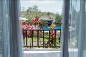 A view from a balcony with a pool, surrounded by tropical plants and a house in the background. - Jepun Sari Uluwatu (Pecatu)