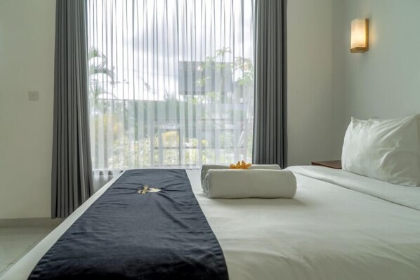 A hotel room with a large bed, a bedside table, a nightstand, and a window with curtains.