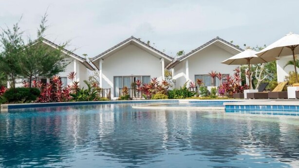 A swimming pool with a clear blue water surface, surrounded by white buildings with large windows, and lush tropical plants. - Jepun Sari Uluwatu (Pecatu)