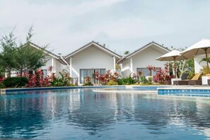 A swimming pool with a clear blue water surface, surrounded by white buildings with large windows, and lush tropical plants.