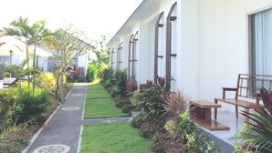 A modern hotel corridor with a pathway, outdoor seating, and lush greenery. - Jepun Sari Uluwatu (Pecatu)