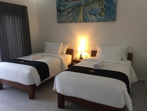 Two single beds with white bedding and black headboards, a bedside lamp, and a large abstract painting on the wall. - Jepun Sari Uluwatu (Pecatu)