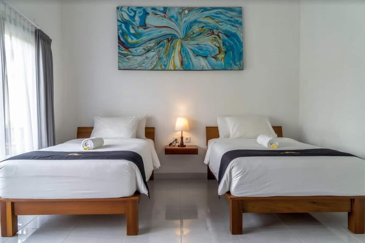 A hotel room with two beds, a nightstand with a lamp, and a large abstract painting on the wall.
