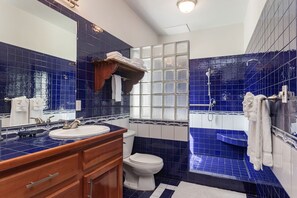 Un baño con azulejos azules, un tocador de madera, un inodoro blanco y una zona de ducha.