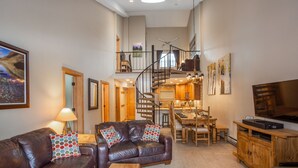 A spacious living room with a leather sofa, a wooden coffee table, and a dining area with a staircase leading to an upper level.