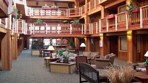 A multi-level hotel lobby with wooden architecture, multiple seating areas, and balconies with plants.