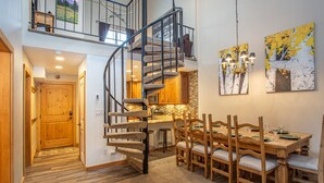 A spacious dining area with a wooden table and chairs, a spiral staircase, and a kitchen area with wooden cabinets.