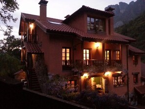 A two-story house with a balcony, multiple windows, and a chimney. - Apartamentos Rurales Buenamadre (Somiedo)