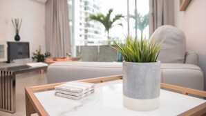 Uma sala de estar moderna com um sofá, uma mesa de centro com livros, um vaso de planta e vista para um edifício através de grandes janelas.