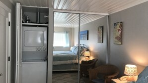 Ein Schlafzimmer mit Bett, Stuhl, Lampe, Kleiderschrank und einem kleinen Tisch.