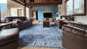 Un salón amplio con un gran tapete azul, sofás de cuero, un mueble de televisión de madera y un balcón con barandilla de madera.
