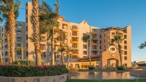 A multi-story hotel with a central courtyard, palm trees, and a pool. - Villa 2206 2BR/3BA Ground Level Condo at Villa La Estancia on Medano Beach (Cabo San Lucas)