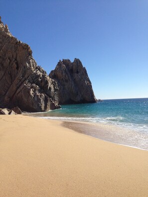 A beach with clear blue water, sandy shore, and rocky cliffs.
