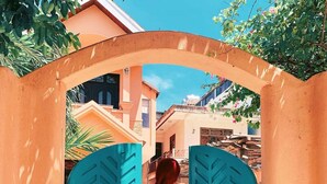 A person walking through a turquoise gate archway into a building with a tiled floor. - The Mansion Hoi An by Minova (Da Nang)