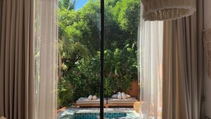A room with a large sliding glass door leading to a pool area, a bed, a small table, and a chair. - The Mansion Hoi An by Minova (Da Nang)
