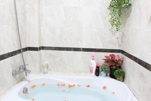 A bathroom with a bathtub, a shower, and a tiled wall with a black border. There are toiletries and a potted plant on the counter. - Bong Gio Apartment (Ho Chi Minh City)