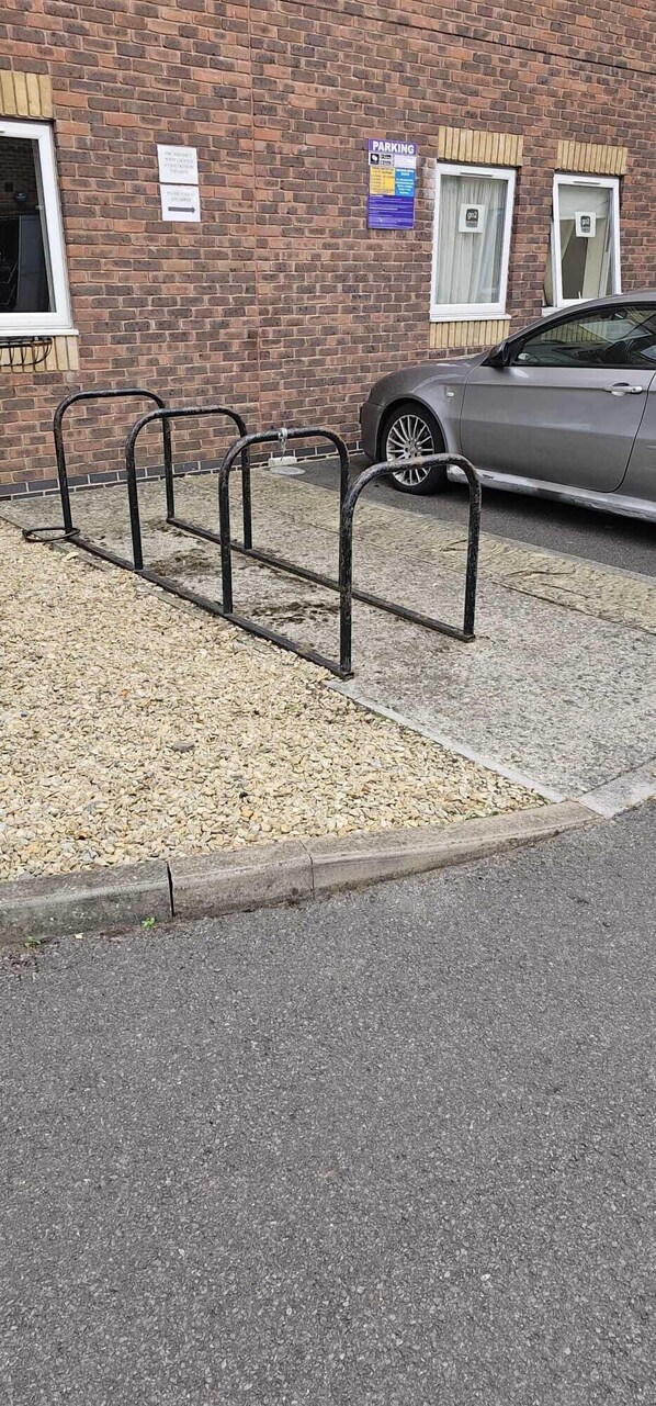 A parking area with a gravel surface and metal bike racks. - GO2 Gloucester Hotel by OYO (Gloucester)