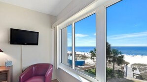 Una habitación con un ventanal grande, un televisor de pantalla plana, una silla roja y un aparador de madera.