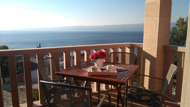 A balcony with a table set for two, a vase with flowers, and a view of the sea. - Apartments San Paaulo (Dugi Rat)