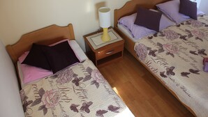 A bedroom with two single beds, each with floral-patterned bedding, a bedside table with a lamp, and a nightstand. - Apartments San Paaulo (Dugi Rat)
