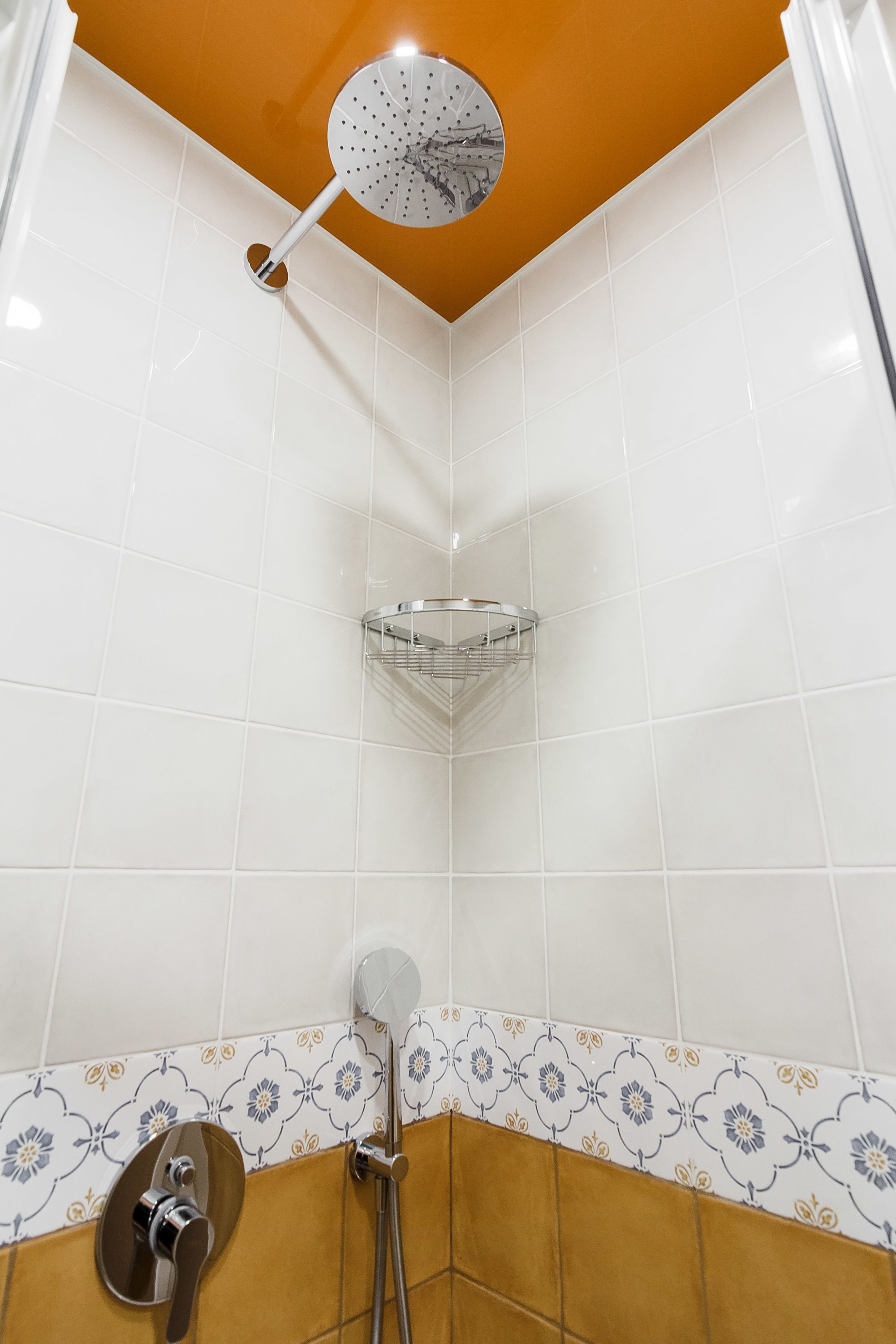 A shower with a ceiling-mounted rain showerhead, a corner shelf, and a wall-mounted faucet.