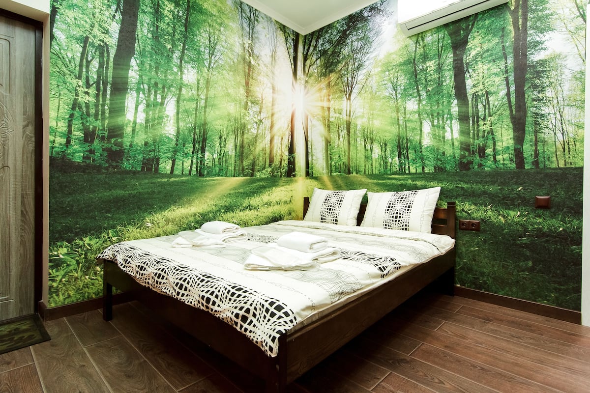 A bedroom with a bed, a large forest mural on the wall, and a wooden floor.