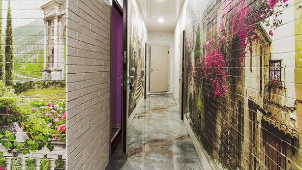 Un pasillo con un mural de un jardín y un edificio, suelo de mármol y una puerta con marco morado.