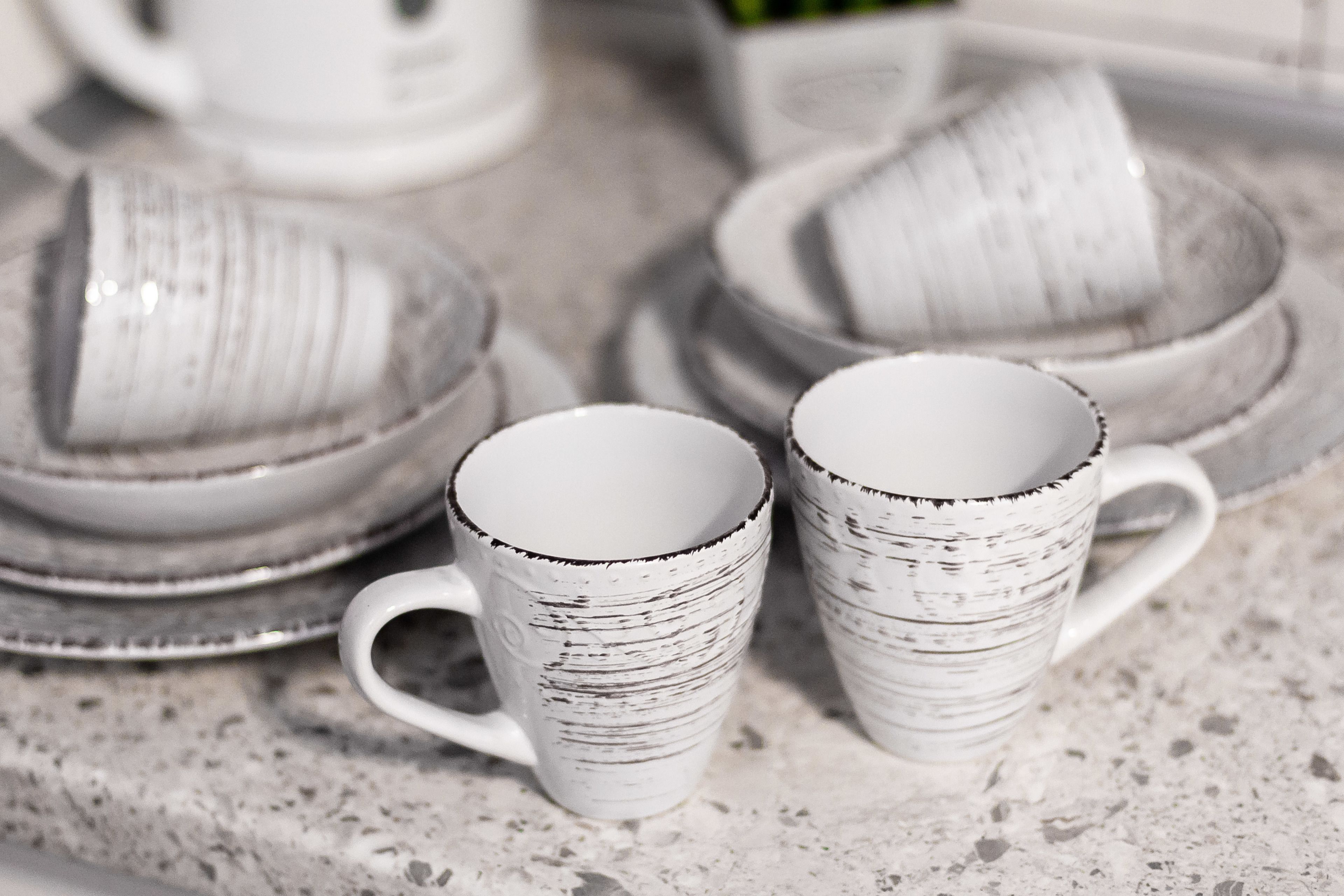 A stack of white ceramic mugs with black speckles on a speckled countertop.
