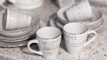A stack of white ceramic mugs with black speckles on a speckled countertop.