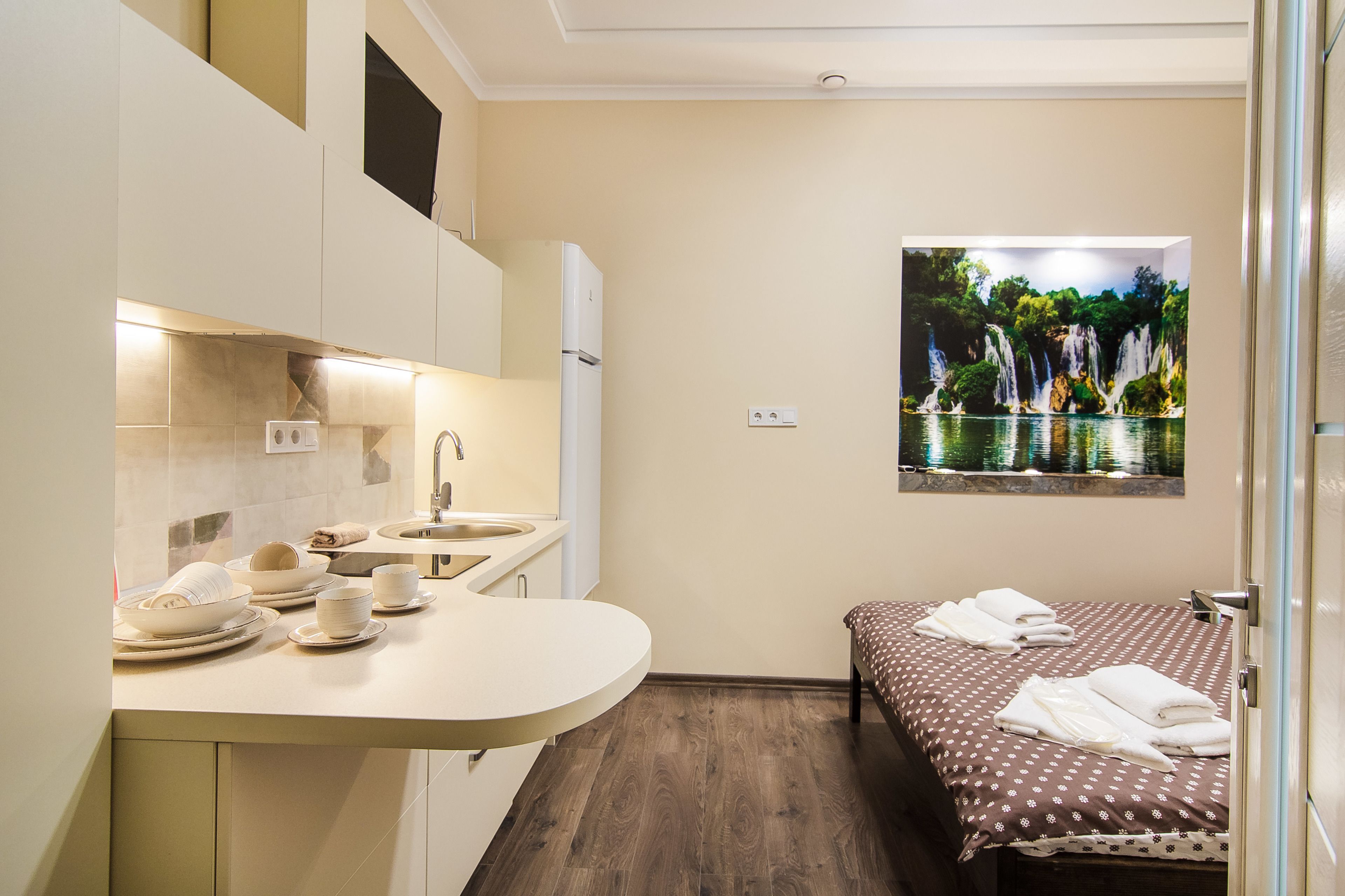 Une chambre d’hôtel compacte dotée d’une kitchenette, d’un lit avec des serviettes et d’une fresque murale représentant un paysage.