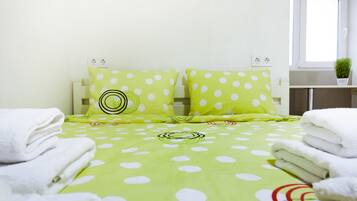 A neatly made bed with a green polka dot bedspread, two matching pillows, and folded white towels on either side.