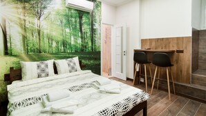 Un dormitorio con un mural de un bosque, una cama con ropa de cama estampada, un escritorio de madera y dos sillas.