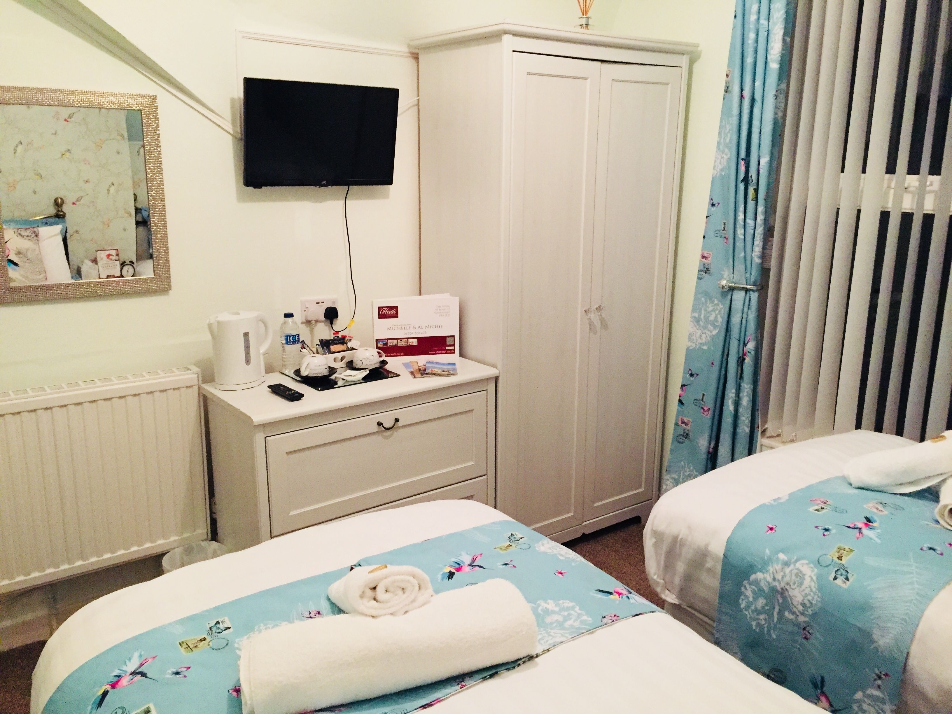 A hotel room with two beds, a television mounted on the wall, a minibar, and a wardrobe.