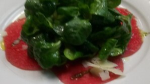 Un plat amb una amanida de fulles verdes i una salsa vermella.
