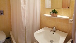 Un bany amb un lavabo blanc, un mirall a la part superior i una estant amb una planta.