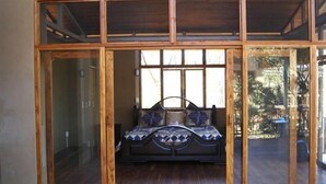 Ein Schlafzimmer mit einem Bett, das unter einem großen Fenster zentriert ist, Holzböden und Blick ins Freie.