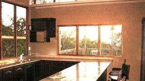 Eine moderne Küche mit einer großen Kochinsel, dunklen Holdschränken und Blick auf eine Terrasse durch große Fenster.